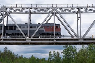 cargo tanker train crossing steel bridge in low view under blue sky on a summer day.