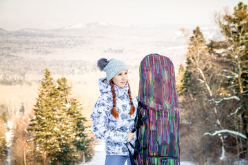 Girl snowboarder standing on a ski track, holding a case with her snowboard and enjoying the ski resort