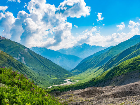 Idyllic landscape with blue sky, fresh green meadows, river and snowcapped mountain top. Svanetia region, Georgia