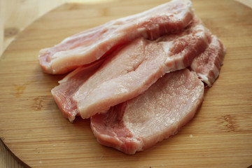 sliced pork steak, fresh pink meat with streaks of fat, on a light wooden Board