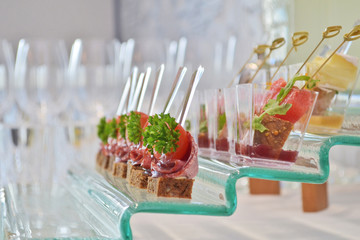Different types of canapes with transparent and wooden skewers on a glass step support on a banquet, side view
