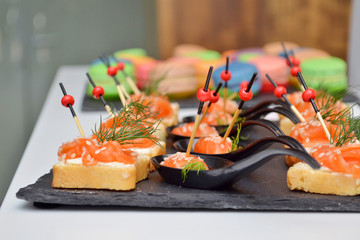 Canape of bread and red fish, lie on a black stone board on the table at the banquet, wooden and glass background