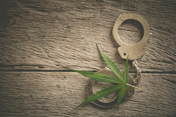 marijuana leaf with iron handcuffs on the background of a wooden table.