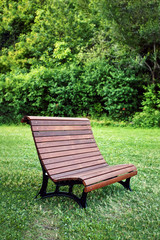 Brown wooden bench on the green grasses of a public park