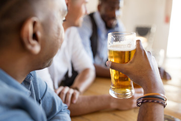leisure and drinks concept - male friends drinking beer at bar or pub