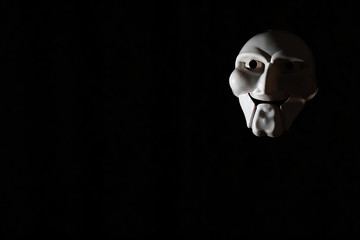 White scary mask on a black background with whites hand.