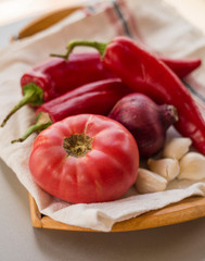 Linen napkin with red chili peppers and garlic cloves with tomato and onion on wooden tray