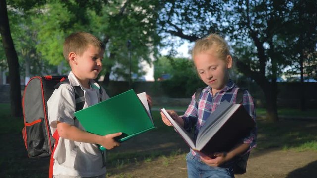 children education, schoolchildren boy and girl with big books in hands read after lessons standing in park