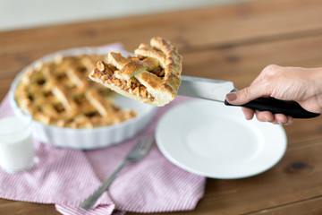 food, culinary and baking concept - close up of hand with piece of apple pie on knife