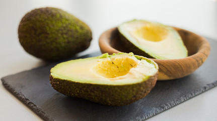 Sliced ripe green avocados in bowl on stone slate, close-up