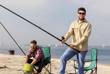 leisure and people concept - male friends with fishing rods on pier at sea