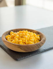 Wooden bowl with pile of yellow corn grains on stone slate, close-up