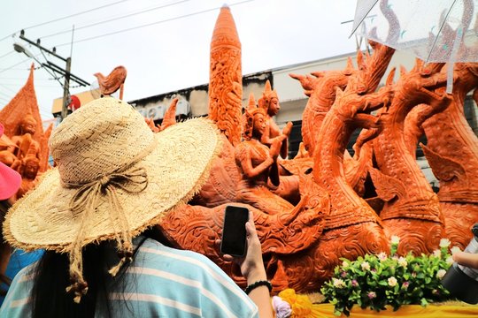 The female tourist take a photo the large candle with mobile phone in Ubon Ratchathani Candle Festival, Thailand. Culture and religion concept.