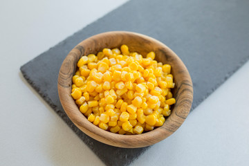 Wooden bowl with pile of yellow corn grains on stone slate, close-up