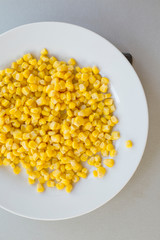 Pile of yellow corn grains with spoon on white plate, close-up