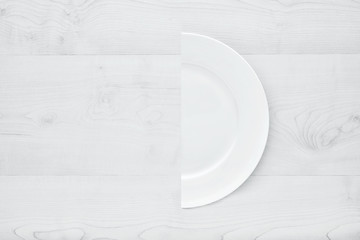 White plate cut in half on white wooden table. Concept of diet.