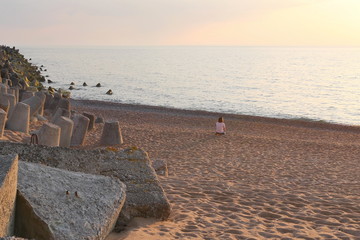 The girl sits on the sandy shore and looks at the beautiful sunset. The problem of loneliness among young people.