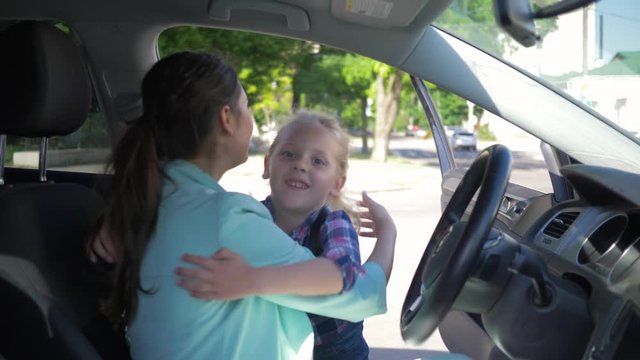 young mother sitting in car meets little schoolgirl from school after lessons and happily hugging