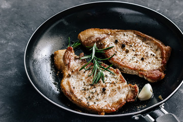 Roasted pork steaks in a frying pan with rosemary and garlic close up.