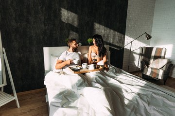 Loving couple having breakfast in bed. Man and woman in bed. Breakfast in bed. Happy couple in bed. The relationship between a man and a woman. Loving couple. Morning lovers. Family relationships.