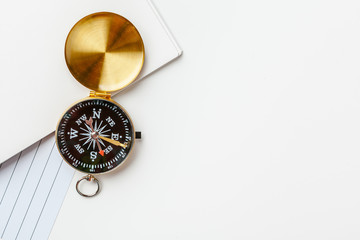 Black notepad for nautical notes and golden compass on a white table