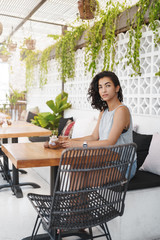 Vertical shot dreamy attractive woman waiting someone coffee table sitting cafe veranda look restaurant entrance curiously checking-out handsome visitor drink coffee contemplate tropical view