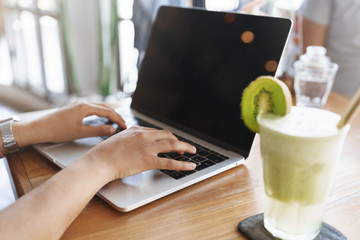 Cropped shot woman hands typing laptop keyboard blank screen, sitting indoor cafe table drink green...