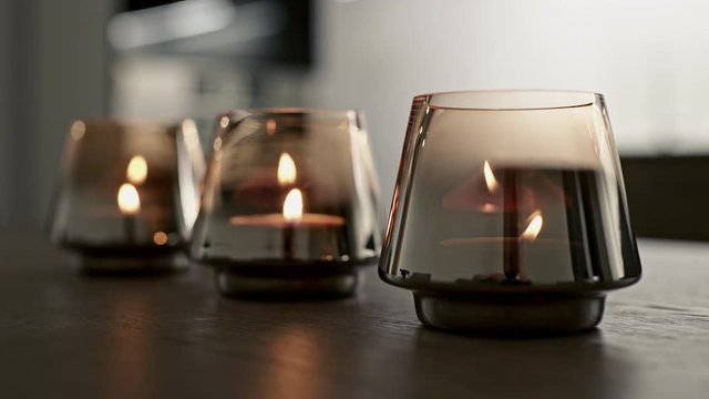 Closeup small candles flaming inside glass holders on lumber table in evening at cozy home. Close up.