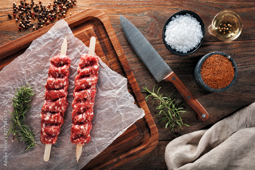 Wall mural raw turkish urfa kebab on white cooking paper and wooden cutting table. dercorated with herbs, spice