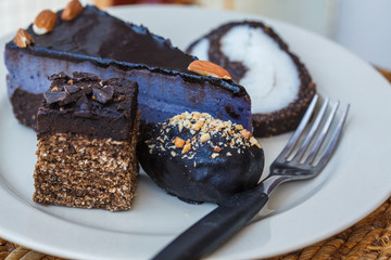 Various vegan desserts on a plate, outside in a cafe. Vegan cheesecake, candy, cake, coconut cake on white plate.