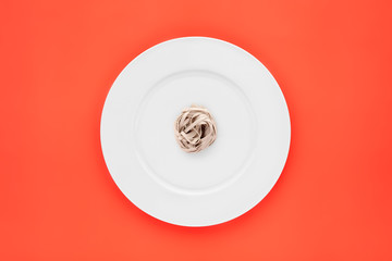 Small portion of tagliatelle pasta on round white plate on orange background. Concept of dieting,...