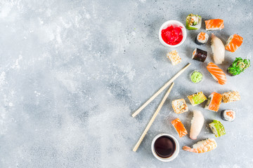 Assorted sushi set on stone or concrete background.  Japanese classic sushi, sushi nigiri. rolls, soy sauce, ginger, chopsticks. Top view. copy space