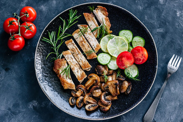 Dish of roasted meat, champignon mushrooms,cucumber and rosemary. Close up. Dark styled photo.