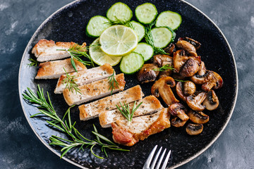 Dish of roasted meat, champignon mushrooms,cucumber and rosemary. Close up. Dark styled photo.