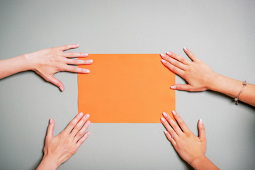 Female hands holding blank orange paper or paper sheet. Gray background. Copy space