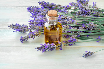 Lavender essential oil in a glass bottle with a bouquet of fresh blooming lavender flowers on a rustic wooden background with a place for text