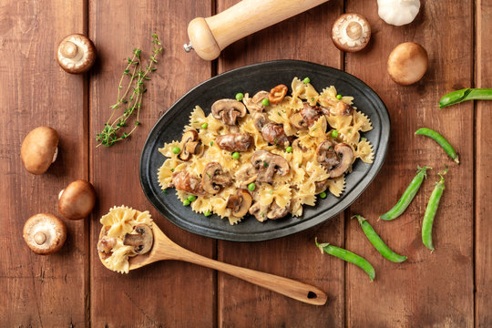 Mushroom and cheese pasta. Farfalle with cremini and green peas, shot from the top with ingredients on a dark rustic wooden background - Powered by Adobe