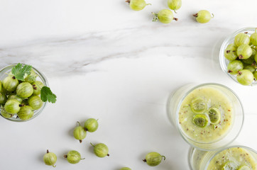 Top view of fresh and tasty gooseberry smoothie, bowls full of ripe sweet and juicy gooseberries on the white table