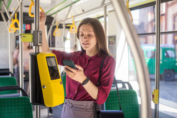 Female Woman paying conctactless with smartphone for the public transport in the tram. Yellow ticket machine in the modern tram