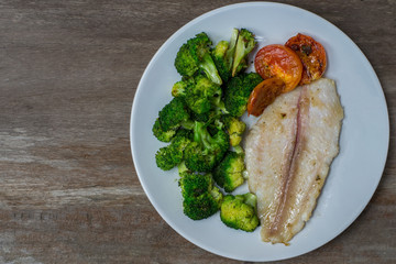 Grilled Fish Fillet with tomato and broccoli vegetables on wood background homemade.