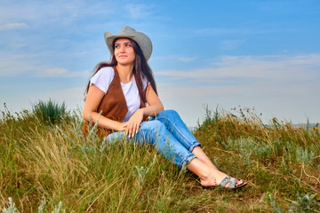 Girl in cowboy dress standing back on the top of Caucasus mountain with a scenery view to sunset at green valley. Female travel nature concept.