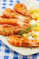 Large grilled shrimps with boiled potatoes on a white plate in a restaurant on the table.