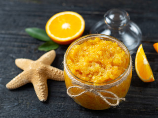 Orange scrub in a glass jar on a wooden table with orange slices and a starfish