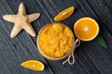 Orange scrub in a glass jar on a wooden table with orange slices and a starfish