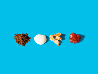 Deconstructed breakfast on blue background. Food elements - ground coffee, yogurt, toasted bread, strawberry jam. Harsh light