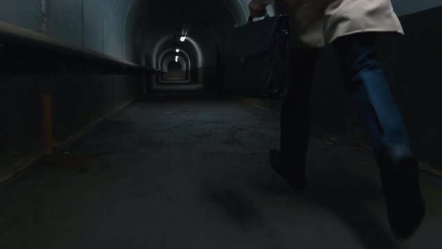 Low-section shot of man in coat with case running in the dark tunnel