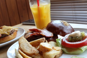 昼食は白い皿に乗ったベーコン、トマト、レタス、肉のハンバーガー。そしてフライドポテトとオレンジジュース。