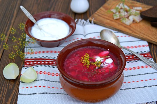 Borscht, hot soup with beets, cabbage and carrots in a clay bowl. Served with sour cream, rye bread and bacon.