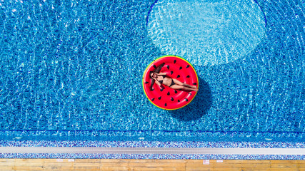 Aerial view of female in bikini lying on a floating mattress in swimming pool with her face covered...