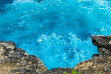 Blue / Turquoise wave is flowing to impact on stone cliff, view from top of the hill side. Location is Nusa Penida island, one of the famous of landmark in Bali - Indonesia. Selected focus.